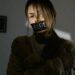 A woman with 'help' tape over mouth, expressing distress and urgency indoors.