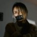 A woman with 'help' tape over mouth, expressing distress and urgency indoors.